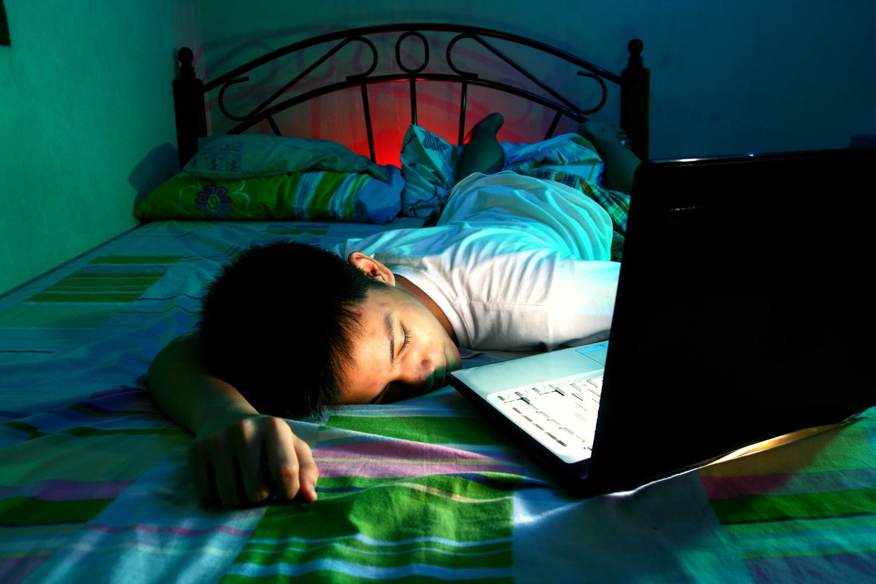 Teen boy asleep on bed with laptop