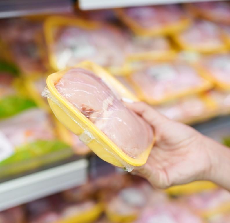 Hand holding packaged chicken in grocery store