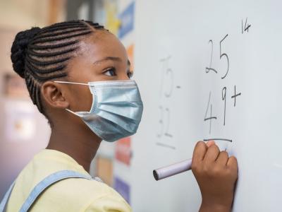Schoolgirl wearing mask writing on whiteboard